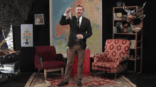 a man in a suit and tie is standing in front of a map and a red chair