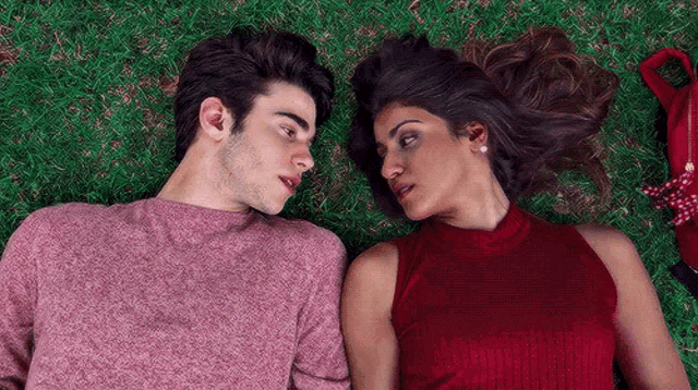 a man and a woman are laying in the grass and looking at each other