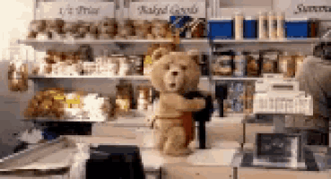 a teddy bear in a red apron is standing in a store