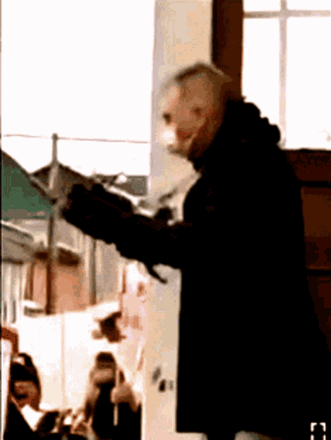 a man in a black coat is holding a gun in front of a window