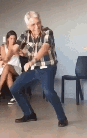 a man in a plaid shirt is dancing in front of a group of people sitting in chairs .