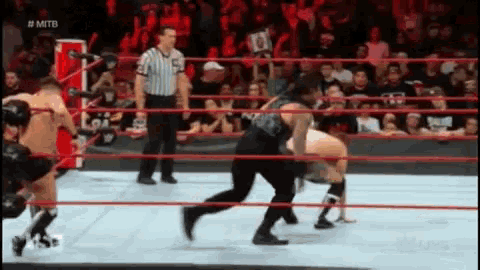 a referee is standing in the middle of a wrestling ring watching two wrestlers fight .