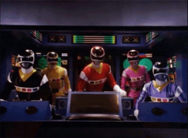 a group of power rangers are standing next to each other in a room with a monitor .