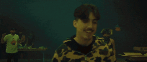 a man in a camouflage jacket is smoking a cigarette in a dark room .