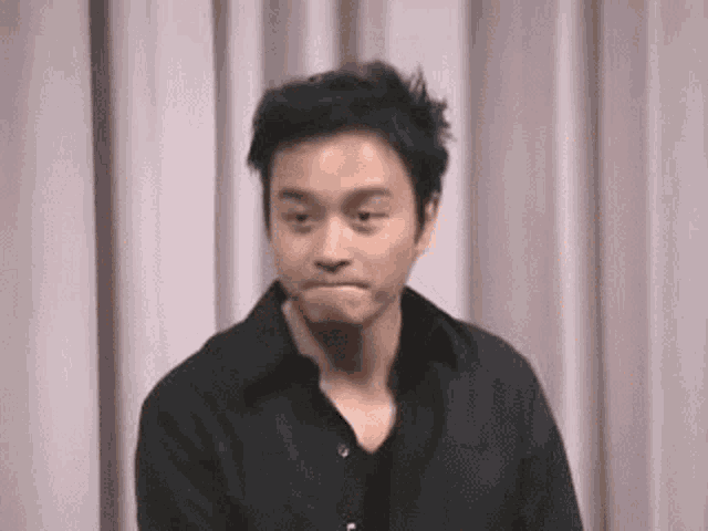 a man in a black shirt is making a funny face while standing in front of a pink curtain .