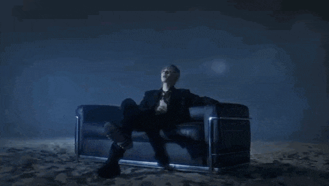 a man with blue hair is sitting in the sand on a couch .