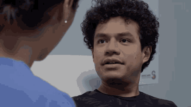 a young man with curly hair is talking to a nurse in a hospital room .