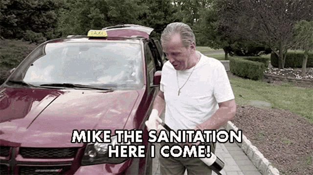a man standing in front of a red taxi that says mike the sanitation here i come .