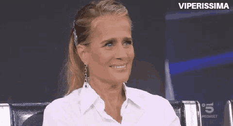 a woman wearing a white shirt and earrings is smiling while sitting on a chair .