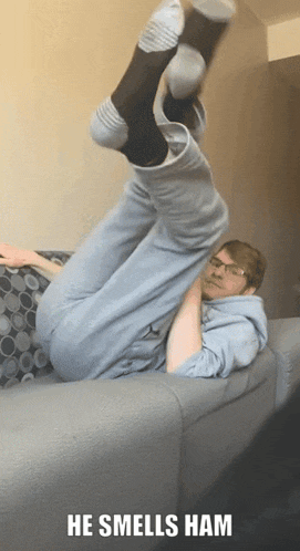 a man is laying on a couch with his legs in the air and the caption he smells ham