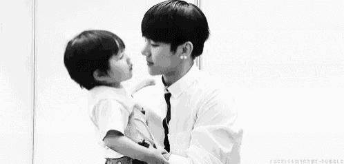 a man is holding a little boy in his arms and kissing him on the cheek .