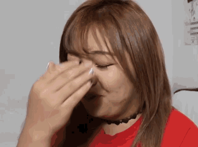 a woman in a red shirt is crying and covering her face with her hands .