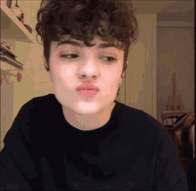 a girl with curly hair is wearing a black shirt and making a funny face