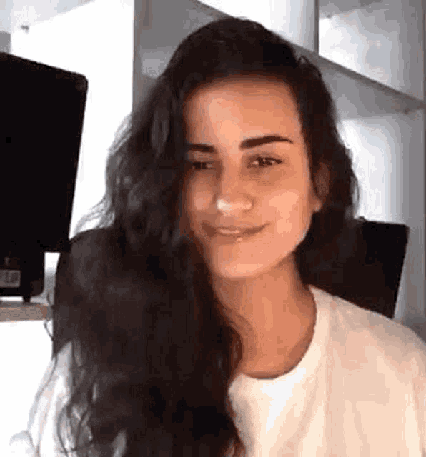 a woman with long dark hair is smiling while sitting in front of a computer screen .