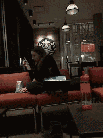 a woman sits on a couch with a laptop in front of a starbucks sign