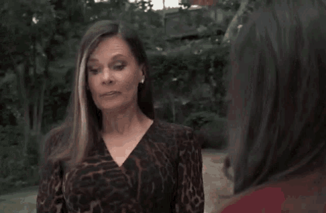 a woman in a leopard print dress is pointing at another woman in a red jacket .