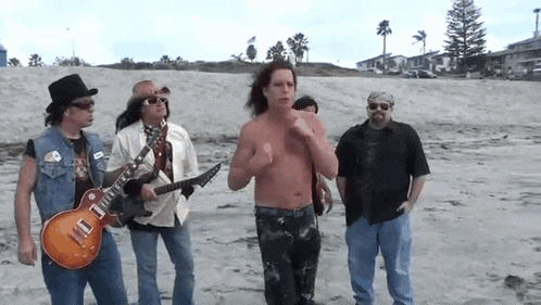 a group of men standing on a beach with one man holding a guitar