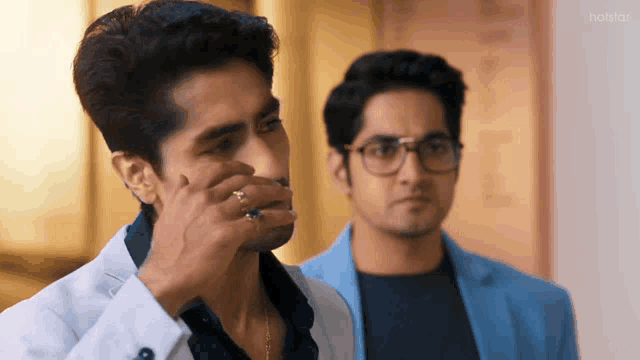 two men are standing next to each other and one of them is covering his mouth with his hand .