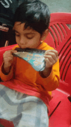 a young boy is sitting in a red chair eating a piece of pizza