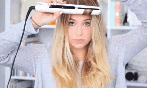 a woman is using a hair straightener on her hair .