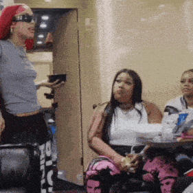a woman with red hair is standing in a room with two other women sitting at a table