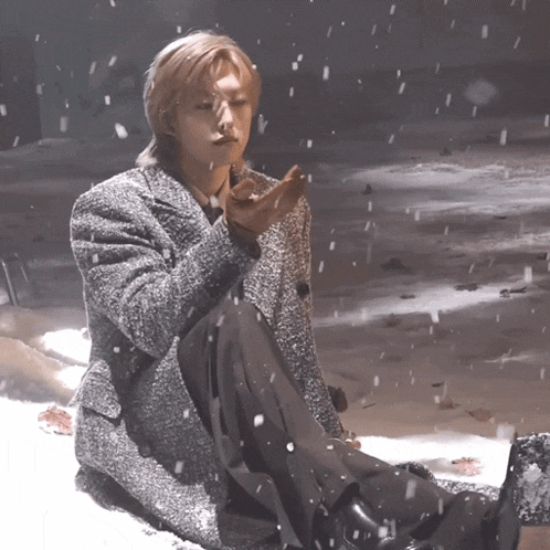 a man in a grey coat is sitting in the snow with snow falling around him