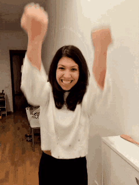 a woman in a white sweater holds her arms up in the air