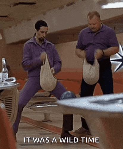 two men are standing next to each other in a bowling alley holding bags .