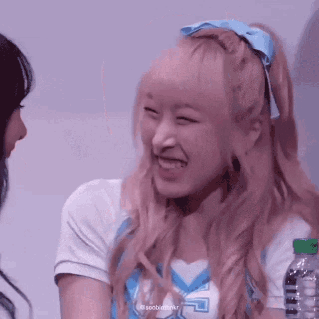 a girl with long blonde hair is smiling and laughing while holding a bottle of water .