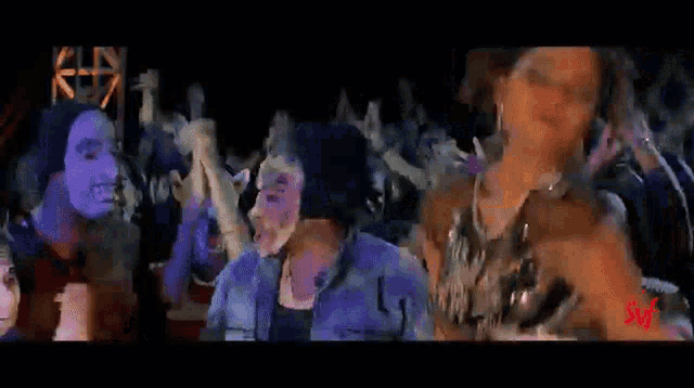 a group of people are dancing in a dark room with a purple light behind them .