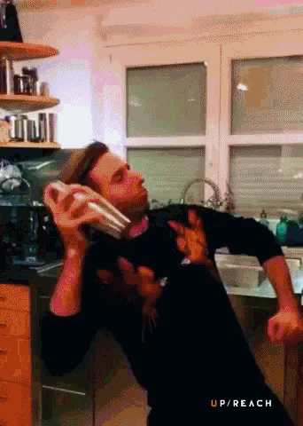a man in a black sweater is talking on a cell phone in a kitchen with the words up / reach below him