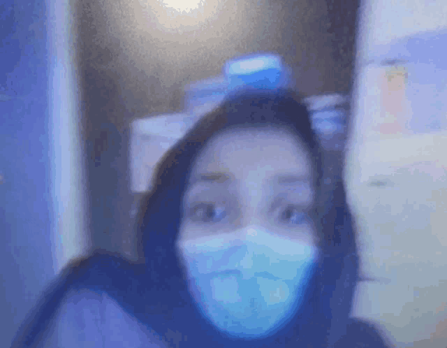 a woman wearing a face mask is standing in front of a computer screen .