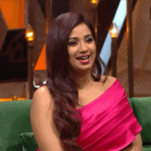 a woman in a pink dress is sitting on a green couch smiling