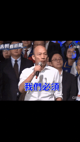 a man is speaking into a microphone in front of a crowd with chinese writing