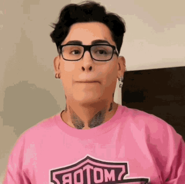 a woman wearing glasses and a pink harley davidson shirt makes a funny face