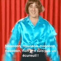 a man in a blue shirt is standing in front of a red curtain and says noooon