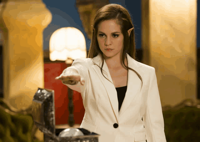 a woman in a white suit is pointing at a treasure chest