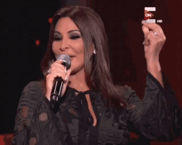 a woman singing into a microphone in front of a tv screen that says on hd