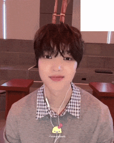 a young man wearing ear buds and a sweater with a yellow chicken on it has his tongue hanging out
