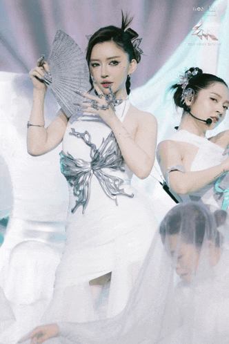 a woman in a white dress holds a fan while another woman stands behind her