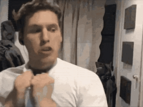 a man in a white shirt is adjusting his tie in front of a mirror