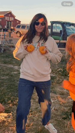 a woman wearing a sweatshirt that says colorado holds two pumpkins in her hands