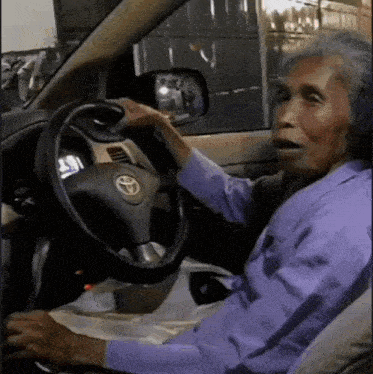 an elderly woman is driving a toyota vehicle