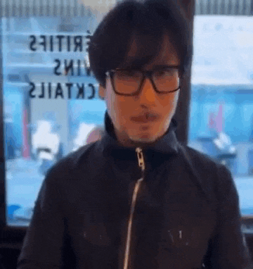 a man wearing glasses and a black jacket is making a funny face .