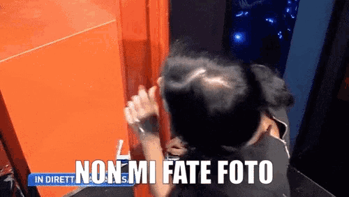 a woman stands in front of an orange wall with the words non mi fate foto on the bottom