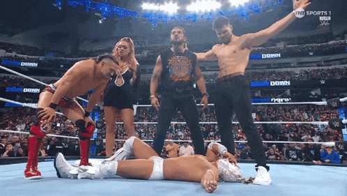 a group of wrestlers are standing around a wrestler laying on the ground