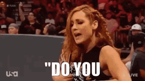 a woman is standing in front of a crowd in a wrestling ring and saying `` do you '' .