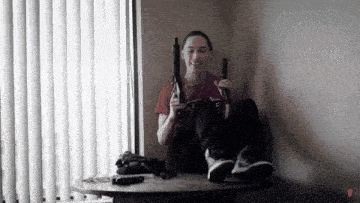 a man sitting on a table holding two guns with a red shirt on