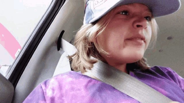 a young girl wearing a purple shirt and a hat with the letter d on it is sitting in a car
