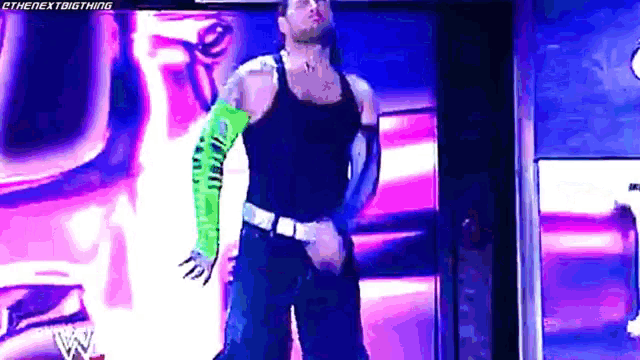 a man in a black tank top and green sleeves is standing in front of a purple background .